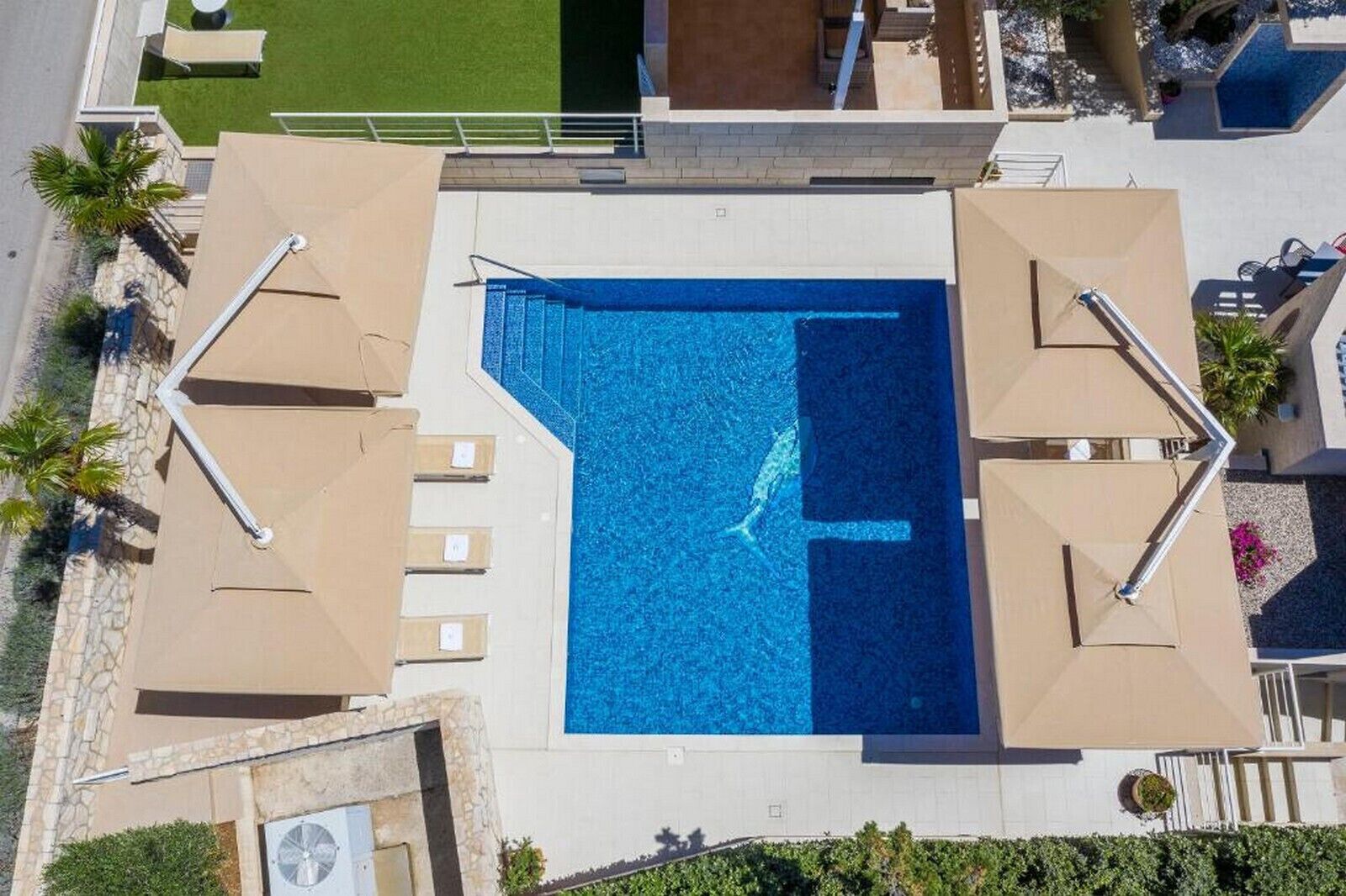 Ein Luftbild eines Schwimmbeckens mit Liegestühlen und einer kleinen Sonnenterrasse.