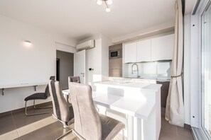 A modern kitchen with white cabinetry, a central island, and a dining area with chairs.