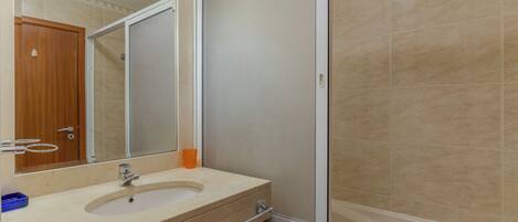 A bathroom with a sink, mirror, and shower enclosure.
