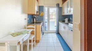 A narrow kitchen with white cabinets, a dining table, and a view through a glass door to the outside. - Ivana Apartment by HR Madeira (Funchal)