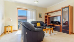 A modern living room with a black leather sofa, a glass coffee table, and a wooden TV stand. - Ivana Apartment by HR Madeira (Funchal)