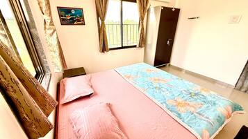 A bedroom with a bed, curtains, a window, a door, and a wall-mounted air conditioner.