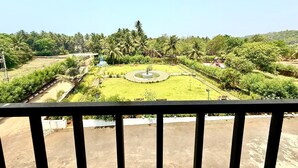 A view from a balcony overlooking a landscaped garden with a central fountain, palm trees, and a playground. - Konkan Pearl Suites (Malvan)