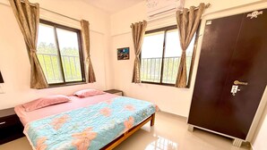 A bedroom with a bed, a wardrobe, a nightstand, and a window with curtains. - Konkan Pearl Suites (Malvan)