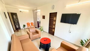 A modern living room with beige sofas, a red coffee table, and a flat-screen TV mounted on the wall. - Konkan Pearl Suites (Malvan)