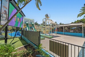 Kids can play on the water slide, climbing wall, and play structure with a slide, surrounded by a secure fence and shaded seating areas.
