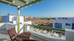 A balcony with a wooden table and chairs, overlooking a coastal landscape with white buildings and a clear blue sky. - Villa Sand Lily with private pool (Naxos)
