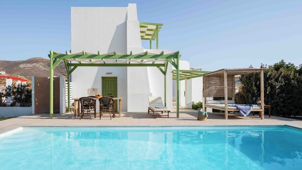 A poolside area with a pergola, a lounge chair, a table with chairs, and a wooden bed structure. - Villa Sand Lily with private pool (Naxos)
