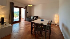 Una sala de estar moderna con comedor, un sofá, una mesa y vistas a una terraza exterior a través de un ventanal corredero.