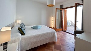 Un dormitorio con cama, lámparas de noche, una lámpara colgante y un ventanal corredero que da a un área exterior.