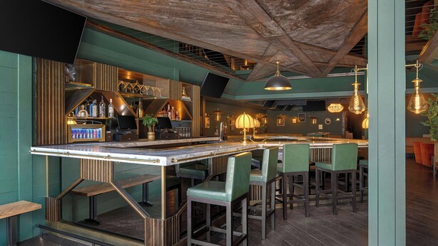 A bar area with a high ceiling, bar stools, and a counter with bottles. - FOUND Hotels, Chicago, Series by Marriott (Chicago)
