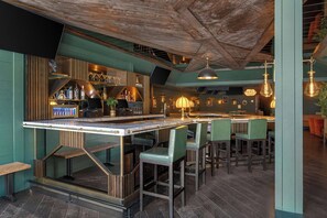 A bar area with a high ceiling, bar stools, and a counter with bottles. - FOUND Hotels, Chicago, Series by Marriott (Chicago)