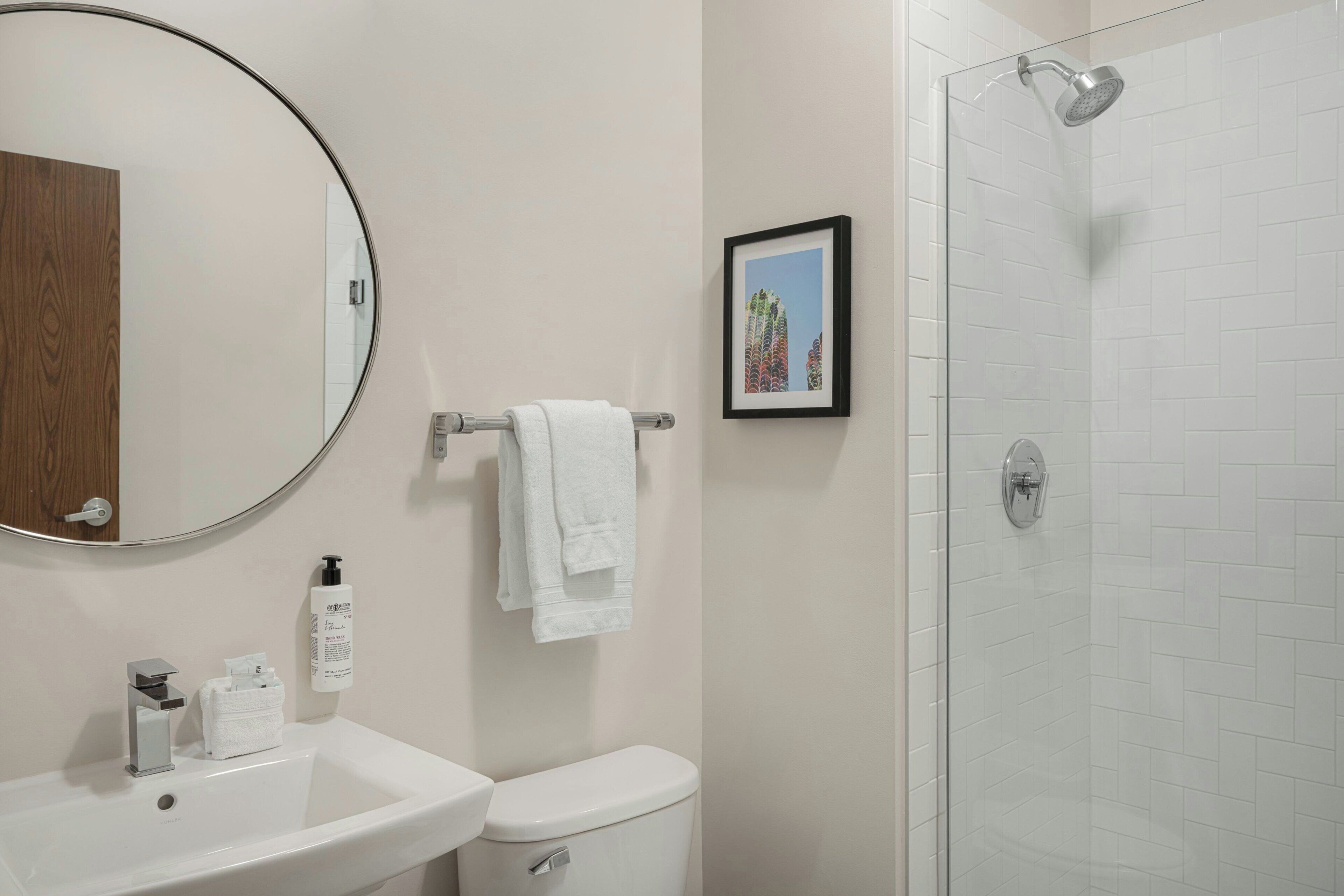 A bathroom with a round mirror, a sink, a toilet, a towel rack, and a framed picture on the wall.