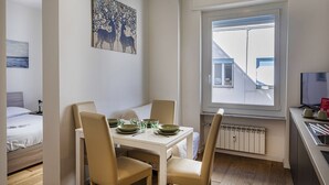 A compact hotel room with a dining area, a bed, a radiator, and a window with blinds. - Zena Tower by Wonderful Italy (Genoa)