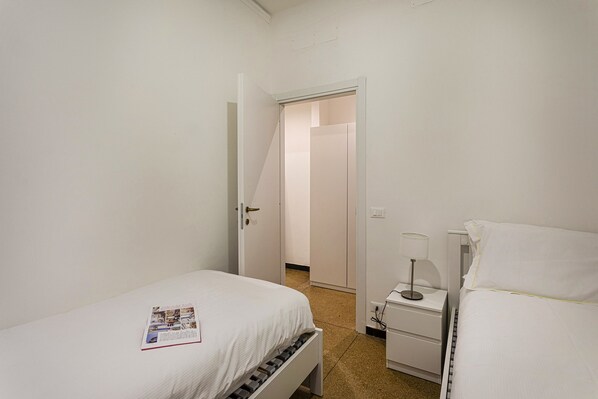 Une petite chambre propre, avec deux lits, une table de chevet avec une lampe et une porte donnant sur une autre pièce.