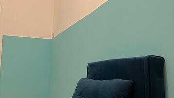 Une pièce avec un seul canapé bleu foncé, placé contre un mur de couleur turquoise, un interrupteur et une prise électrique sur le mur.
