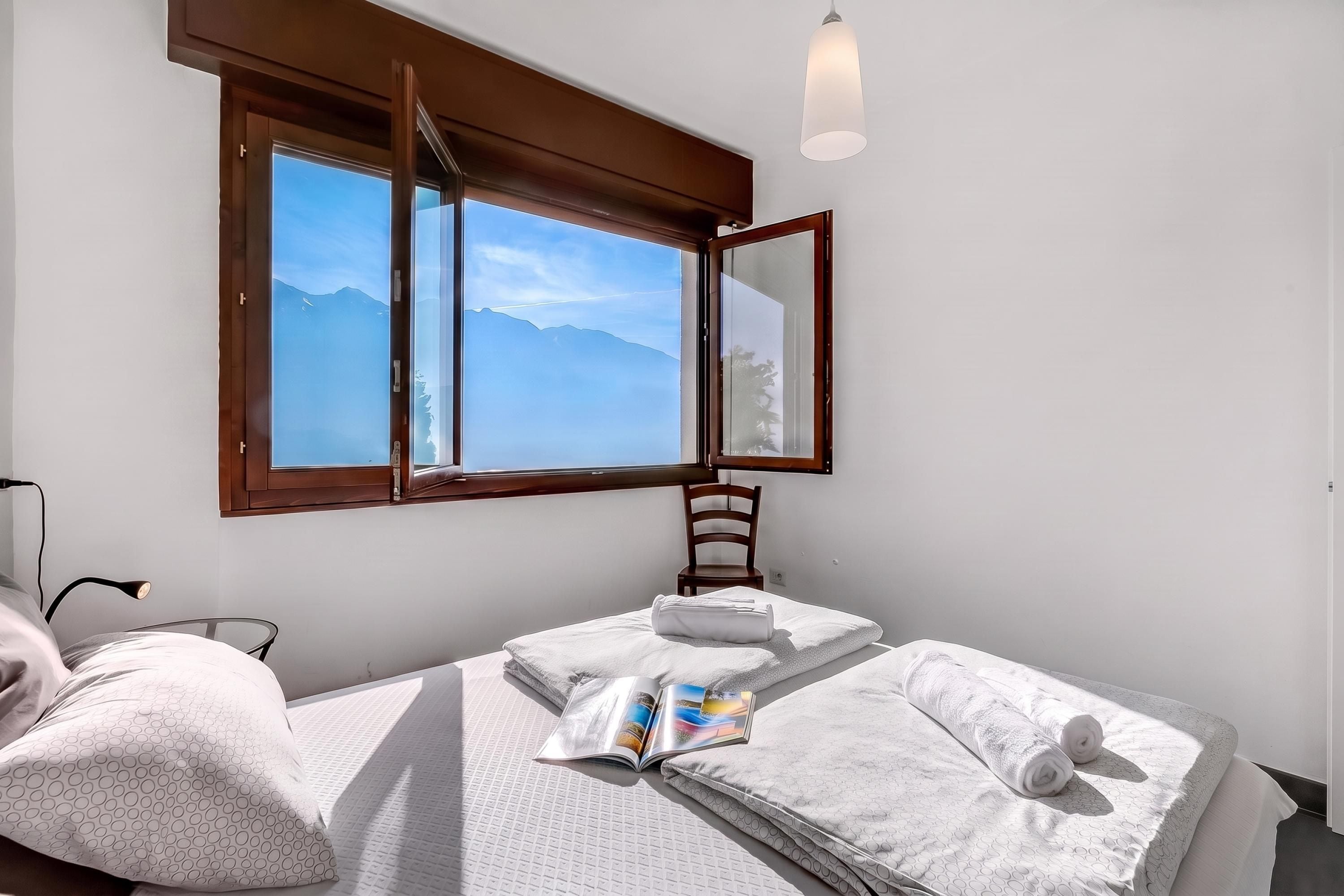 A room with a bed, a chair, a table, and a window with a view of mountains.