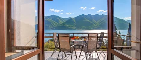 Un balcon avec une table dressée pour deux personnes, offrant une vue sur un lac et des montagnes.