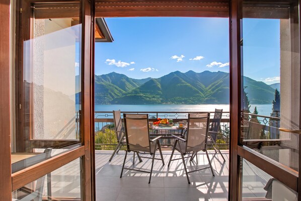 Un balcon avec une table dressée pour deux personnes, offrant une vue sur un lac et des montagnes.