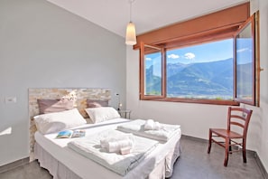 A bedroom with a bed, a chair, a window with a mountain view, and a hanging light fixture.