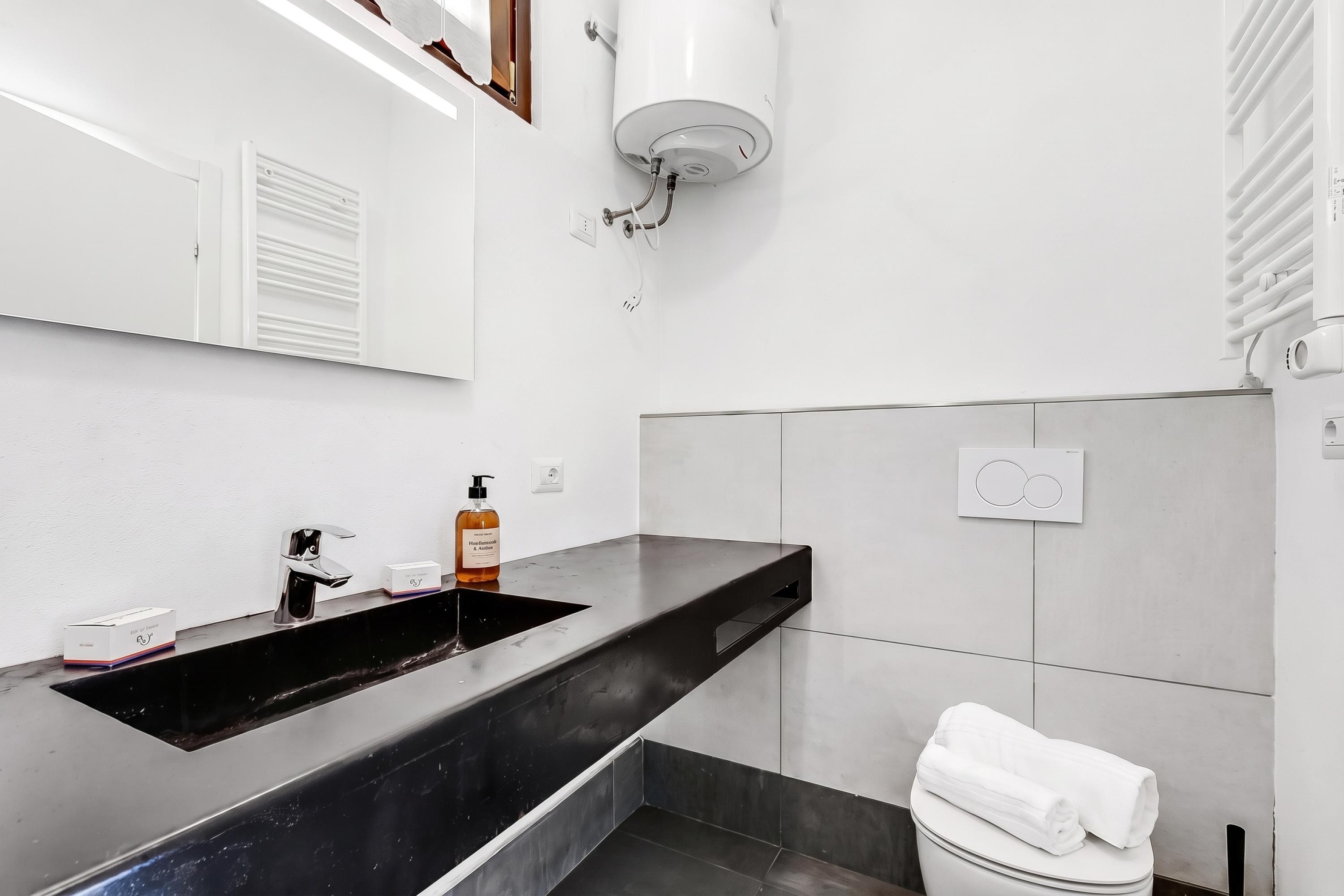 A modern bathroom with a black sink, a handheld showerhead, and a towel on the toilet.