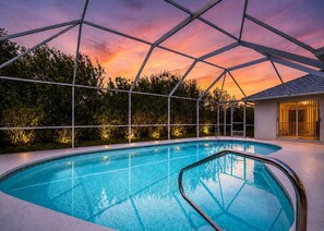 Una piscina con cerramiento de vidrio, rodeada de vegetación y vistas al atardecer.