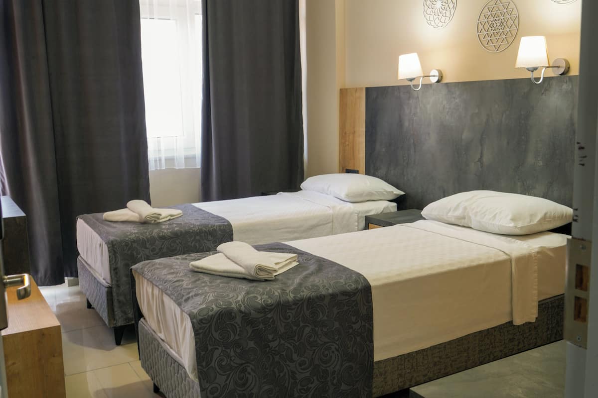 Habitación de hotel con dos camas, cada una con una colcha estampada y almohadas blancas. Hay lámparas de pared y un adorno decorativo sobre las camas.