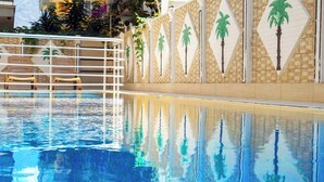 Una piscina d'aigua cristal·lina blava, envoltada per una paret de rajola amb motius de palmeres.