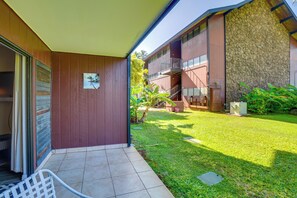 Un edificio moderno con un patio cubierto, una pared de piedra y un pequeño jardín con un banco y plantas.