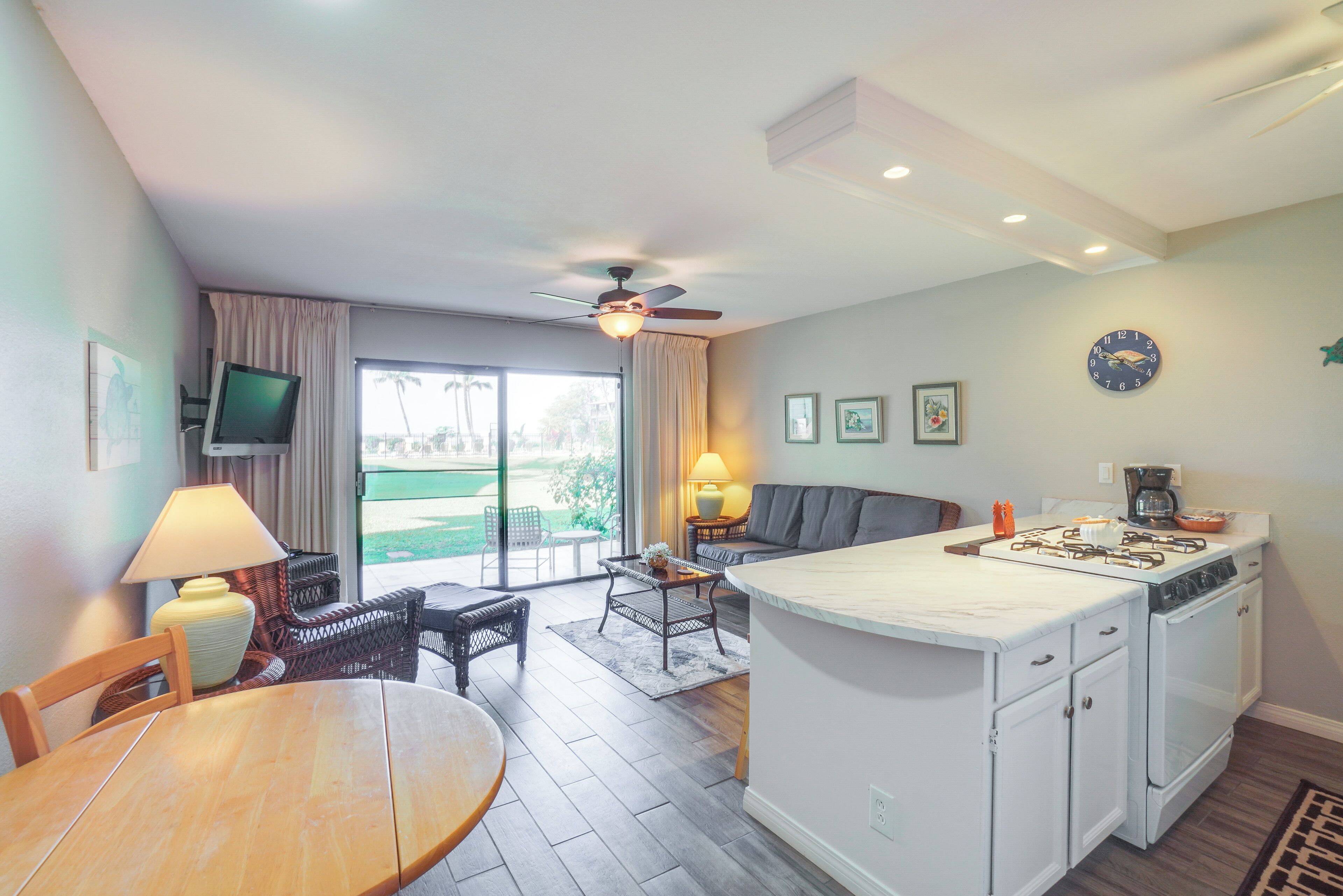 A modern kitchen with a central island, a dining area with a table and chairs, a sofa, and a ceiling fan.