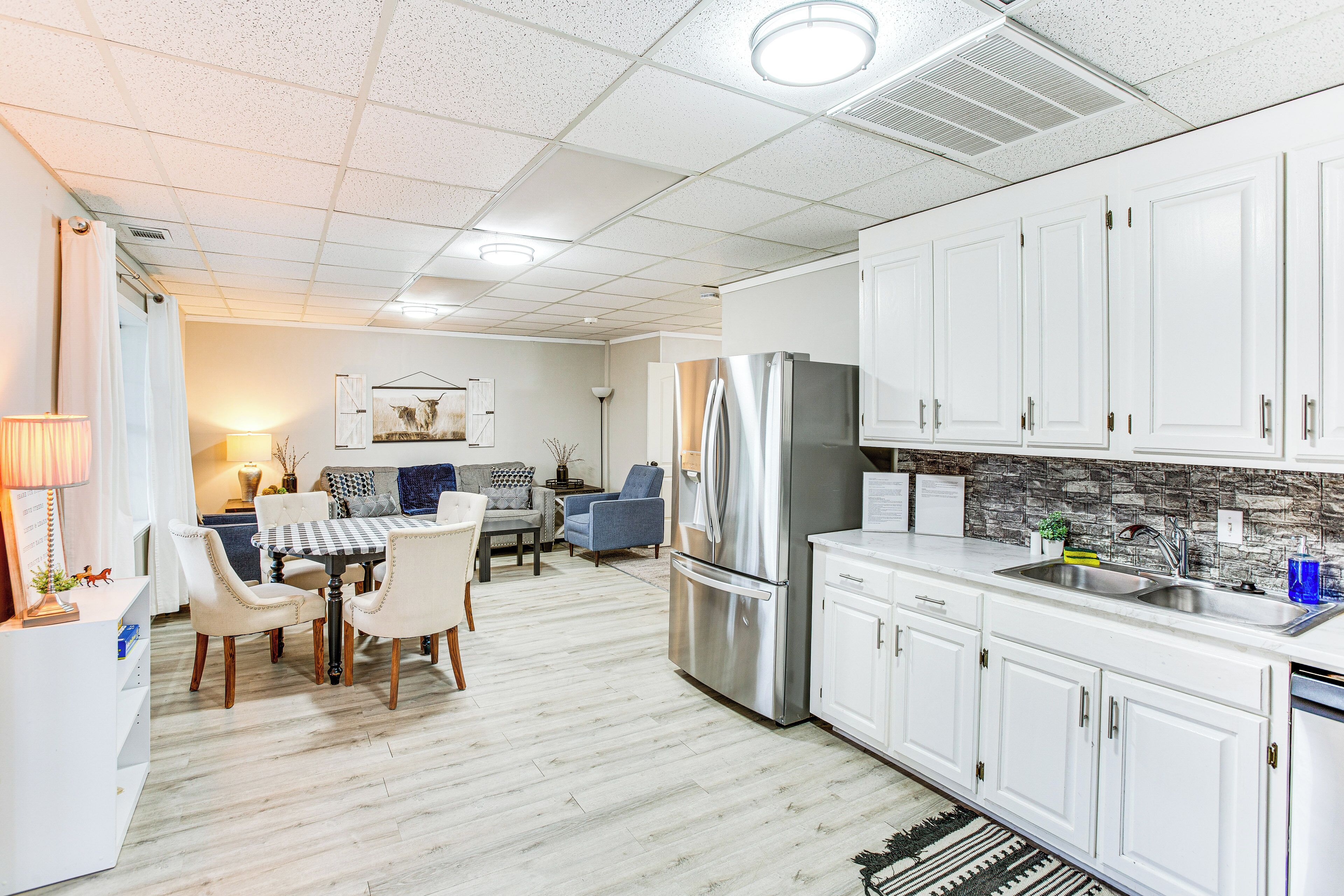 A modern kitchen with white cabinets, a stainless steel refrigerator, and a dining area with a table and chairs.
