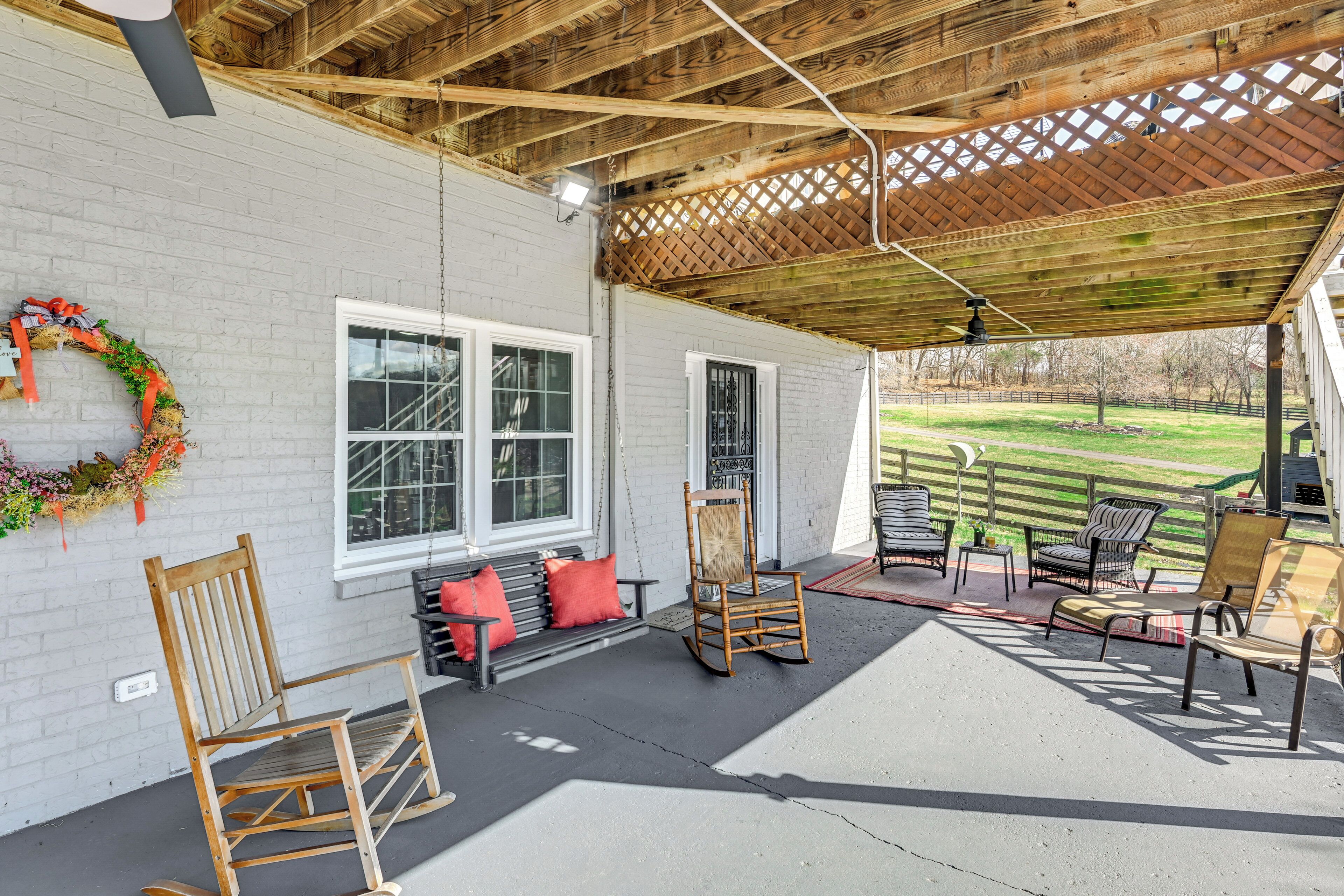 A covered patio with wooden furniture, a white brick wall, and a view of a grassy area.