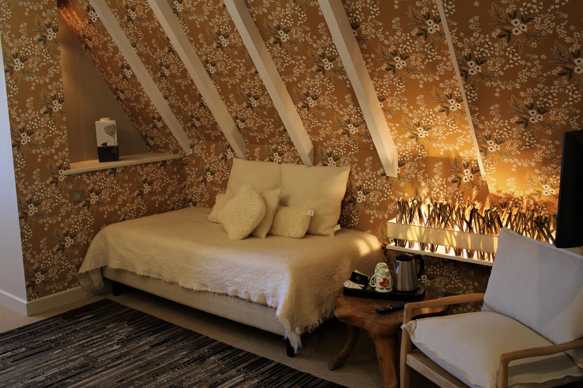 Ein Schlafzimmer mit einem Bett, einem Nachttisch mit Lampe, einem Sessel und einem Regal mit Dekoration.
