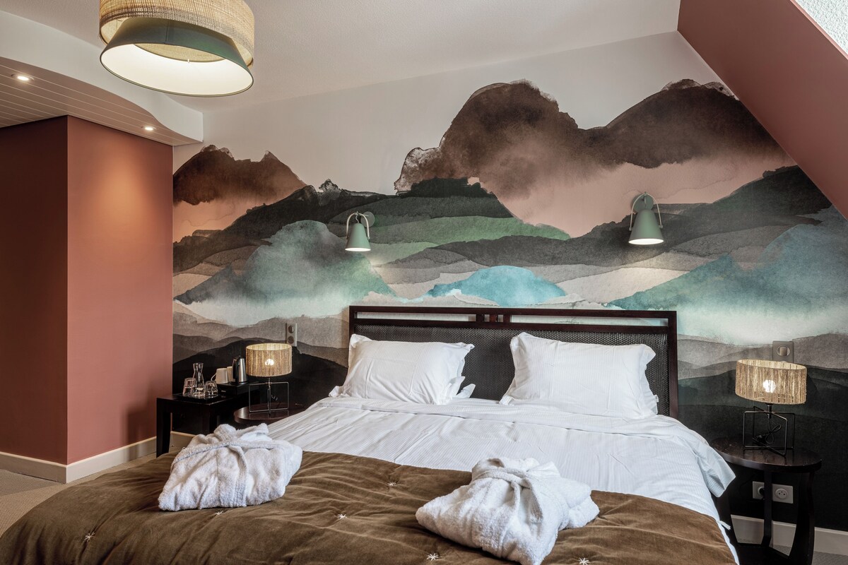 Ein Hotelzimmer mit einem Bett, zwei Nachttischlampen, einem Nachttisch und einer Wandmalerei von Bergen.