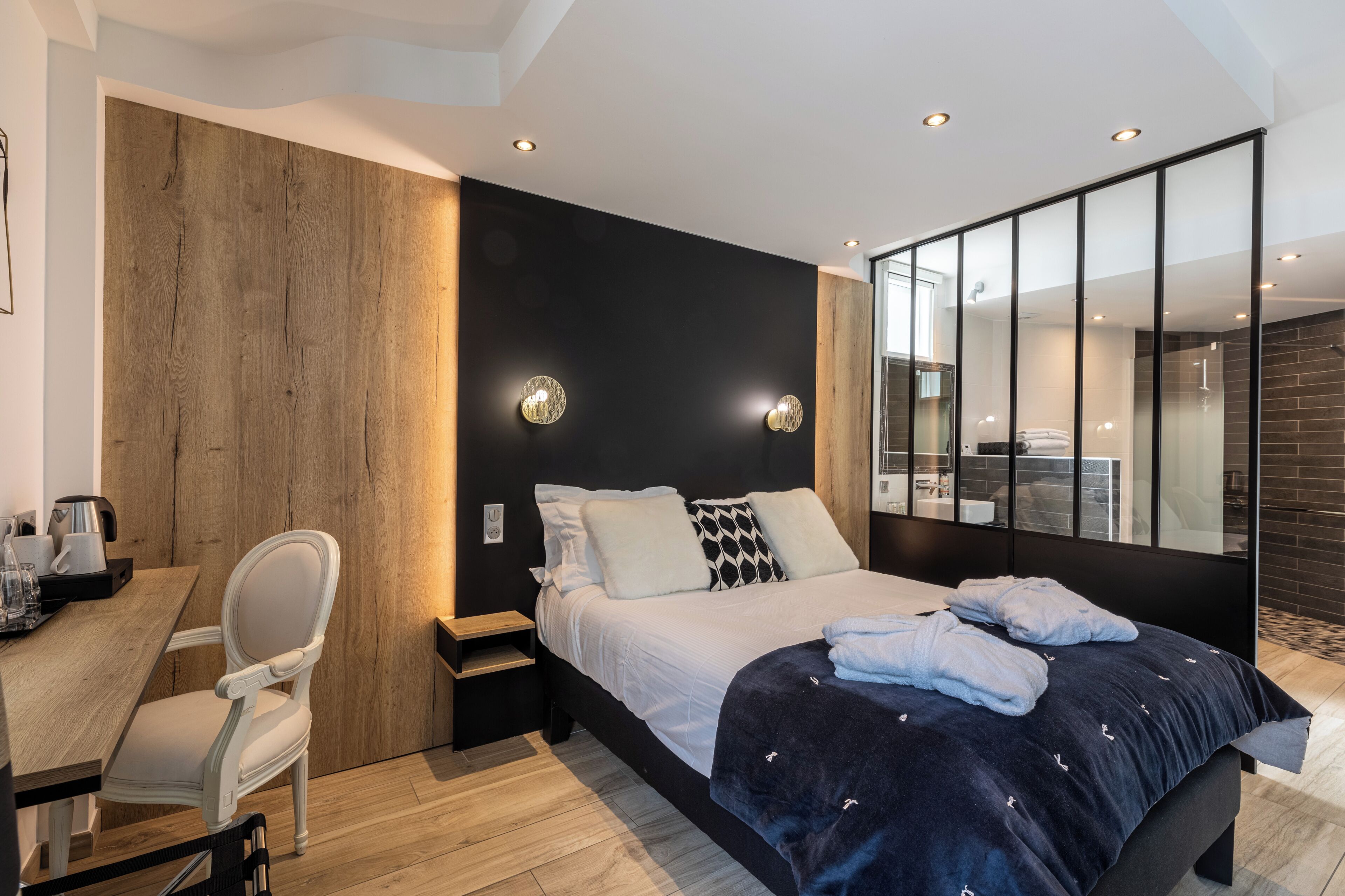 Quarto de hotel moderno com uma cama grande, uma escrivaninha com cadeira, um painel de parede em madeira e um espelho amplo.