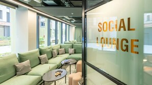 A modern social lounge with green sofas, small round tables, and a glass wall displaying "SOCIAL LOUNGE". - Student Only Winfield Court (Nottingham)