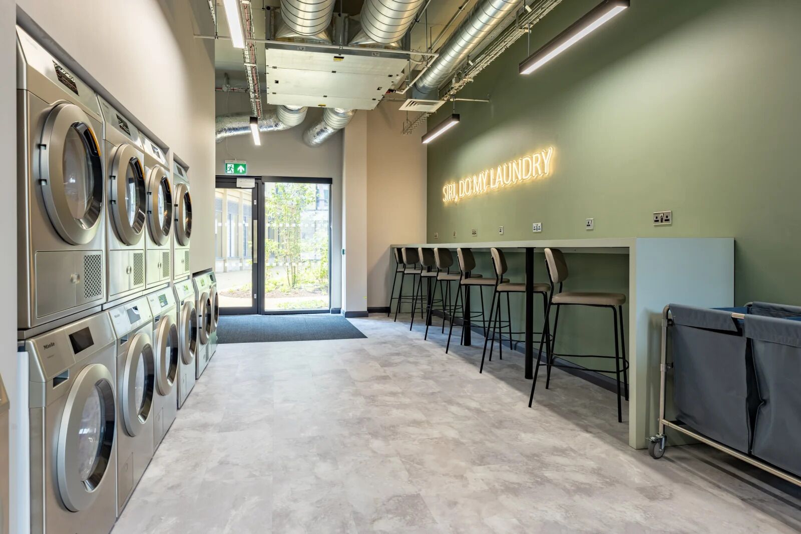 A modern laundromat with multiple washing machines, a seating area, and a wall-mounted sign.