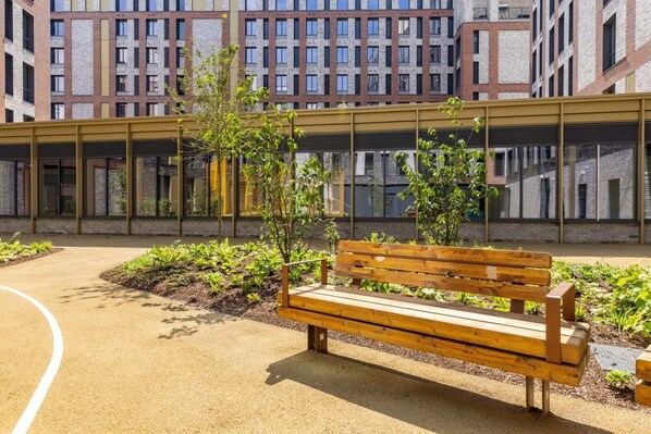 A modern building with a covered walkway, a wooden bench, and a garden area with plants. - Student Only Winfield Court (Nottingham)