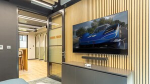 A modern office space with a television displaying a blue car, a gaming room sign, and a seating area with ottomans. - Student Only Winfield Court (Nottingham)
