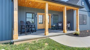 A covered porch with wooden pillars, outdoor seating, and a door leading to the house. - Walk to the Amish Village: Spacious Ronks Getaway! (Ronks)