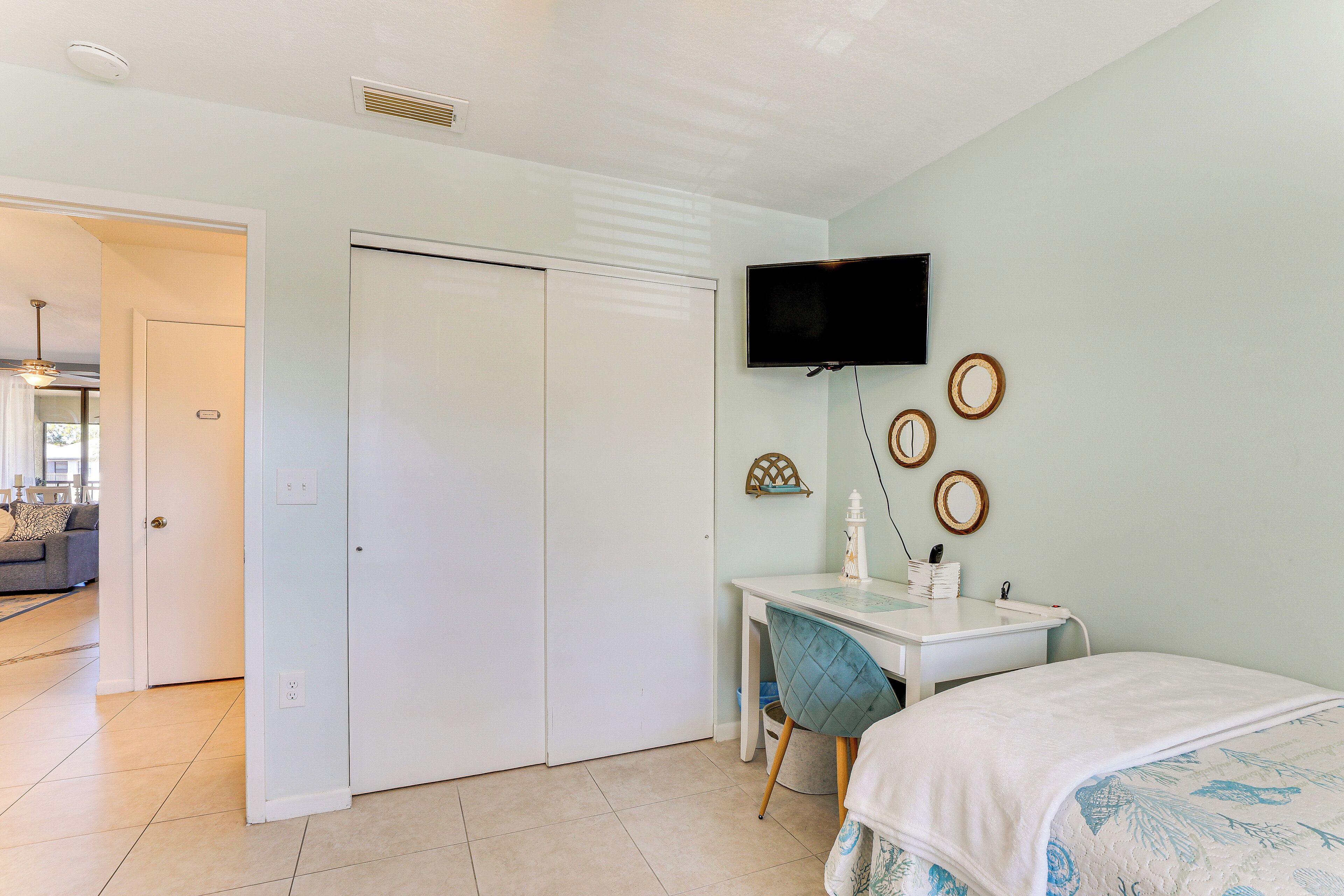 Un dormitorio con cama, escritorio con silla, televisión montada en la pared y puerta que da a otra habitación.