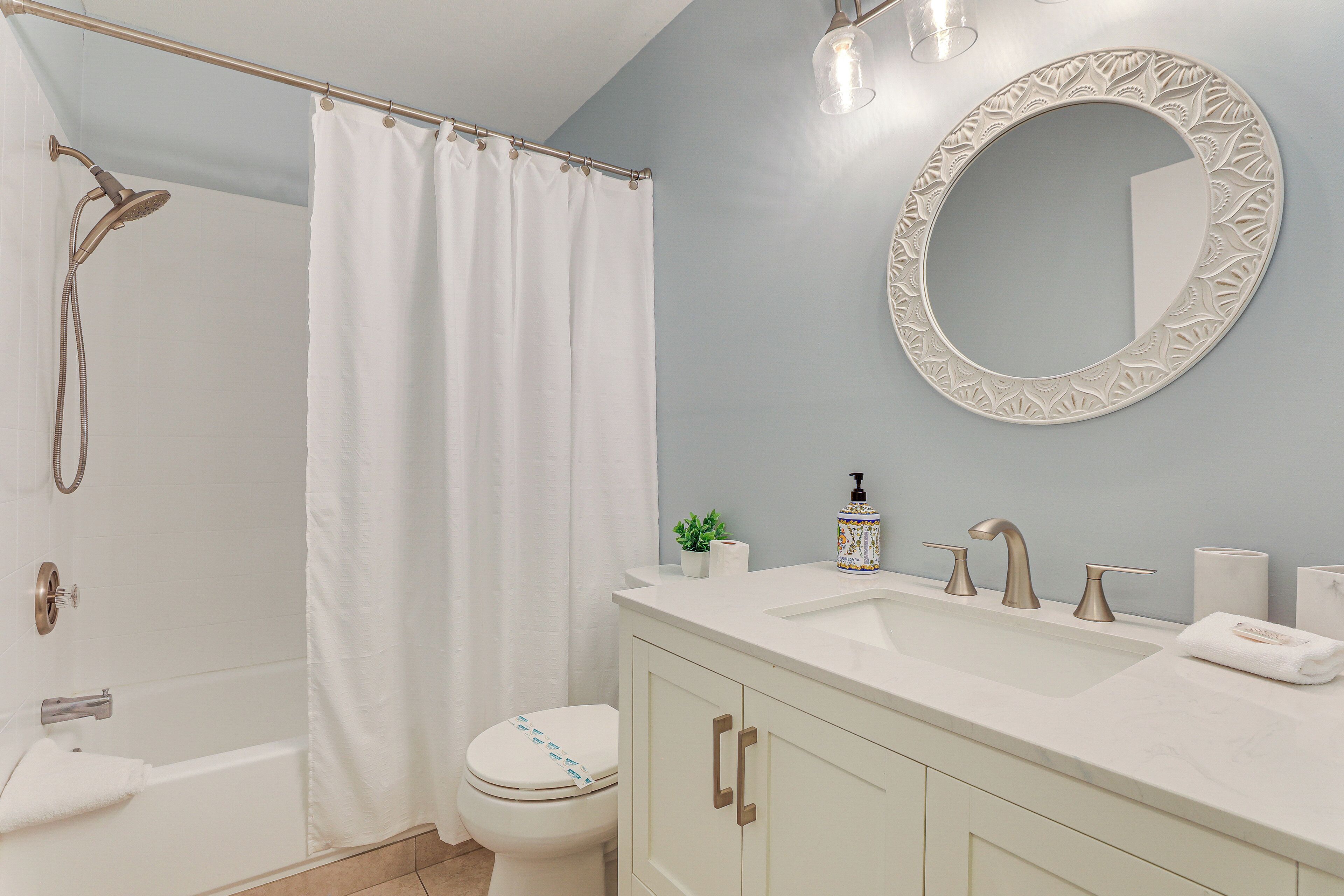 A bathroom with a shower, toilet, sink, and mirror.