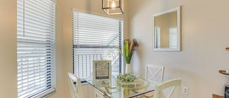 A dining area with a glass table, white chairs, and a hanging light fixture.