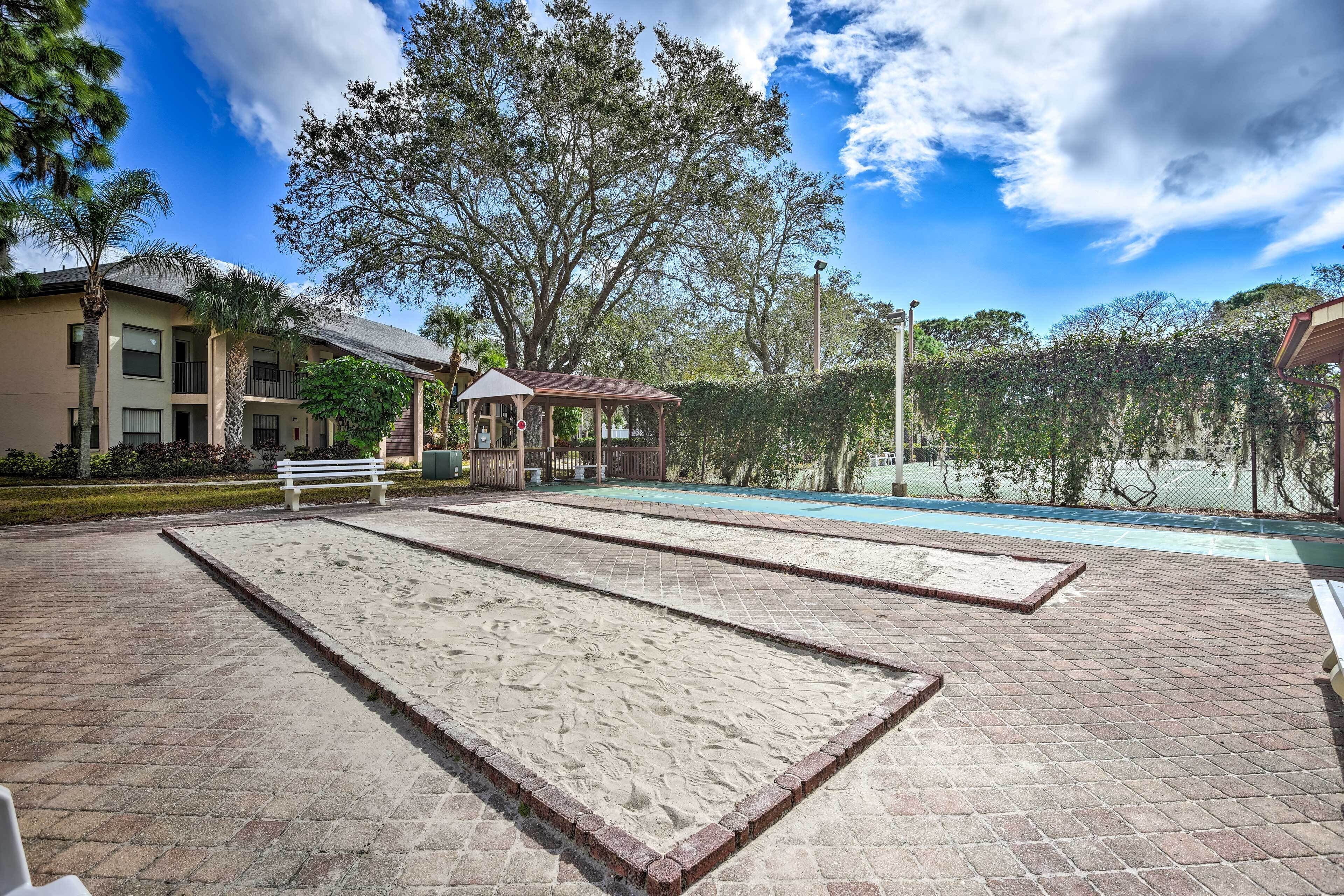 Un área de piscina con una zona de juegos de arena, un pabellón y un edificio al fondo.