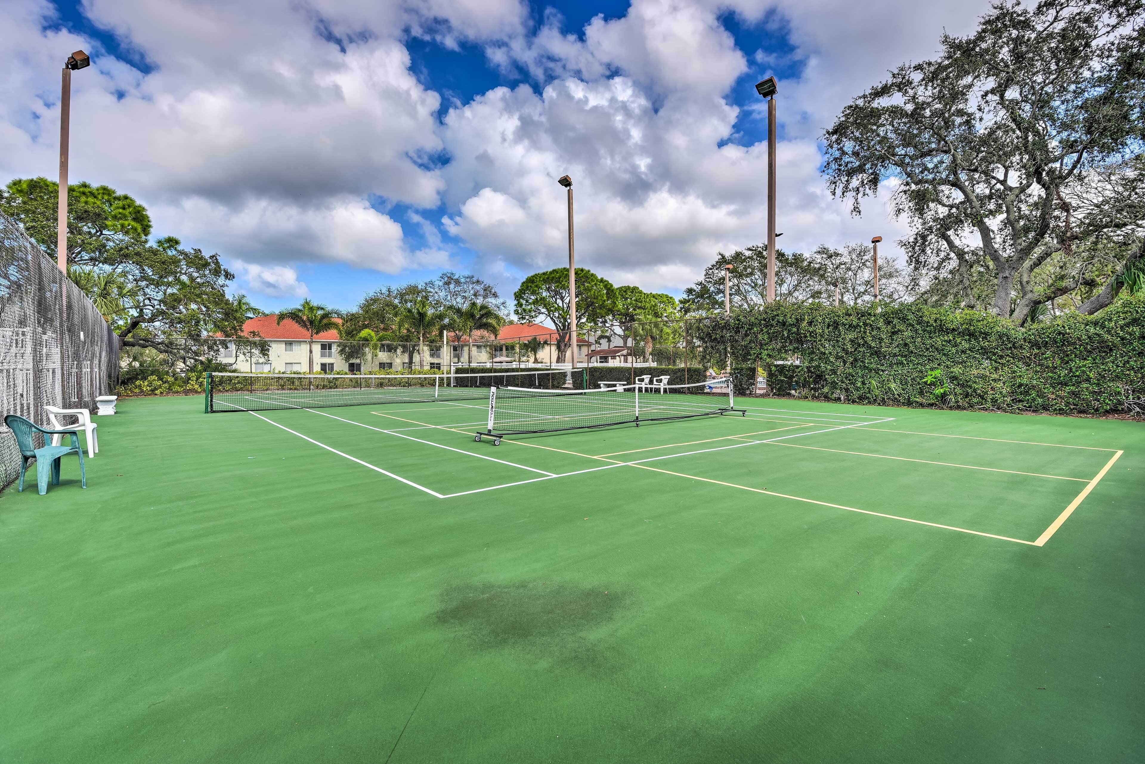 A tennis court with a net, surrounded by trees and a fence.