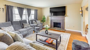 A living room with a grey sofa, a coffee table with books, a fireplace, and a TV. - 3 Mi to Berkshire Mall: Suburban Stay w/ Yard! (Sinking Spring)