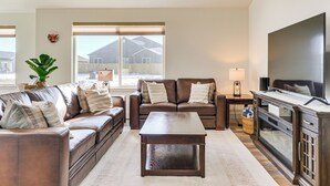 A living room with two brown leather sofas, a wooden coffee table, a TV cabinet, and a large window with a view of a house and mountains. - 2 Mi to Beaverhead River: Family-friendly Home! (Dillon)