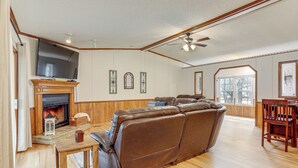 A living room with a fireplace, leather sofa, wooden table, and a television mounted on the wall. - < 1 Mi to Greers Ferry Lake: Dog-friendly Home! (Higden)