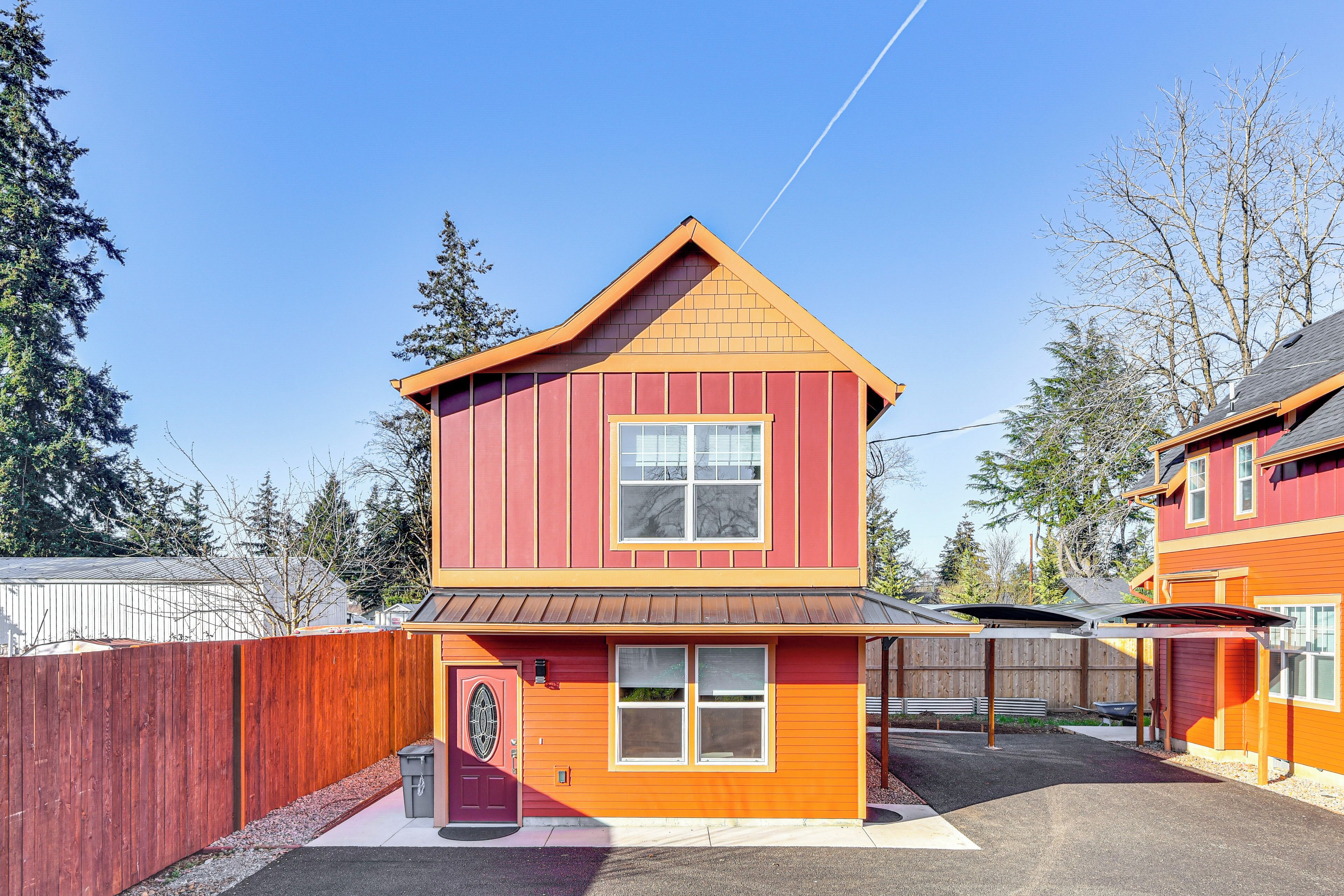 Une maison à deux étages, avec une façade rouge et un toit marron, comprenant un garage et un patio couvert.