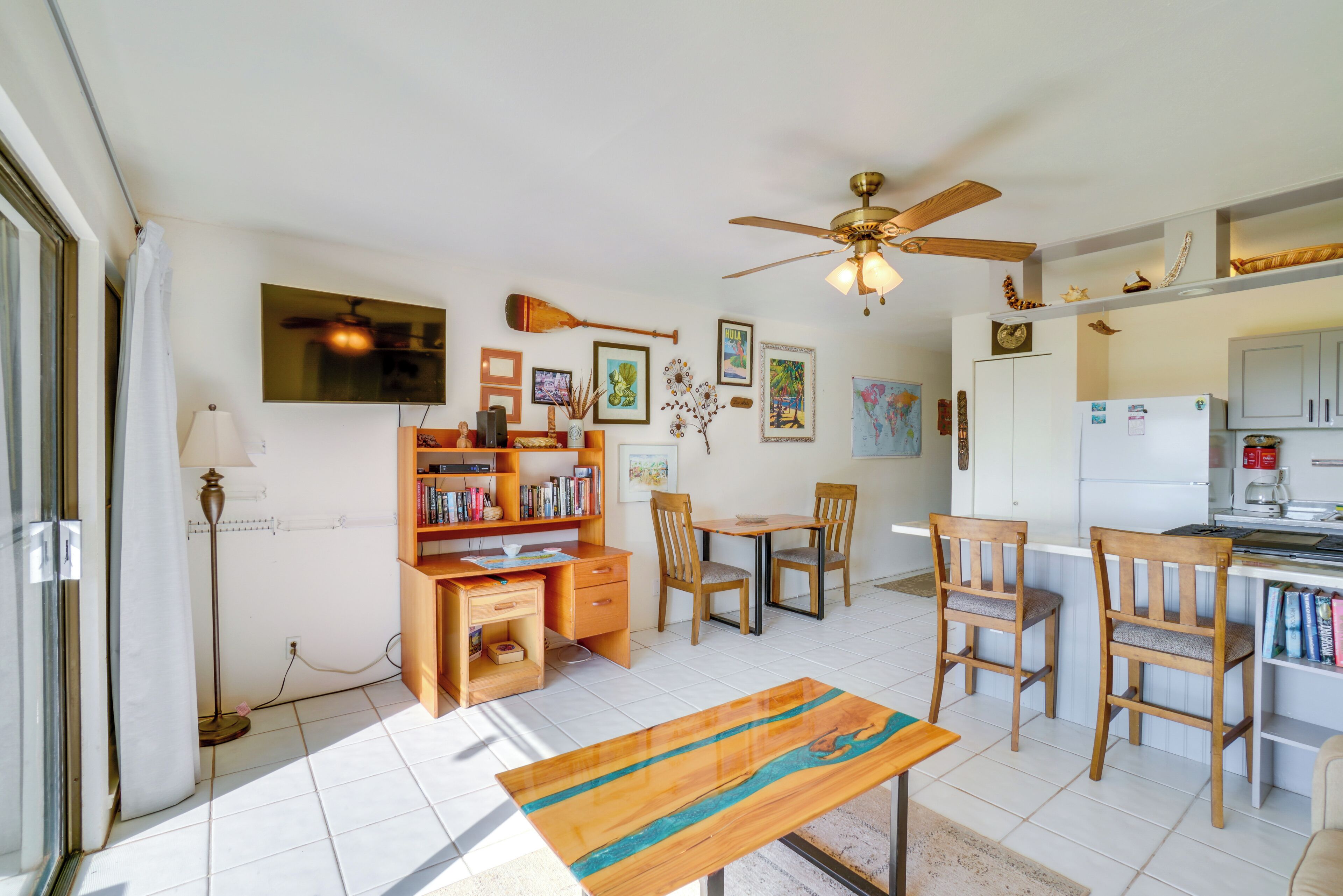 Un espacio habitable compacto con zona de comedor, cocina, ventilador de techo y estantería.